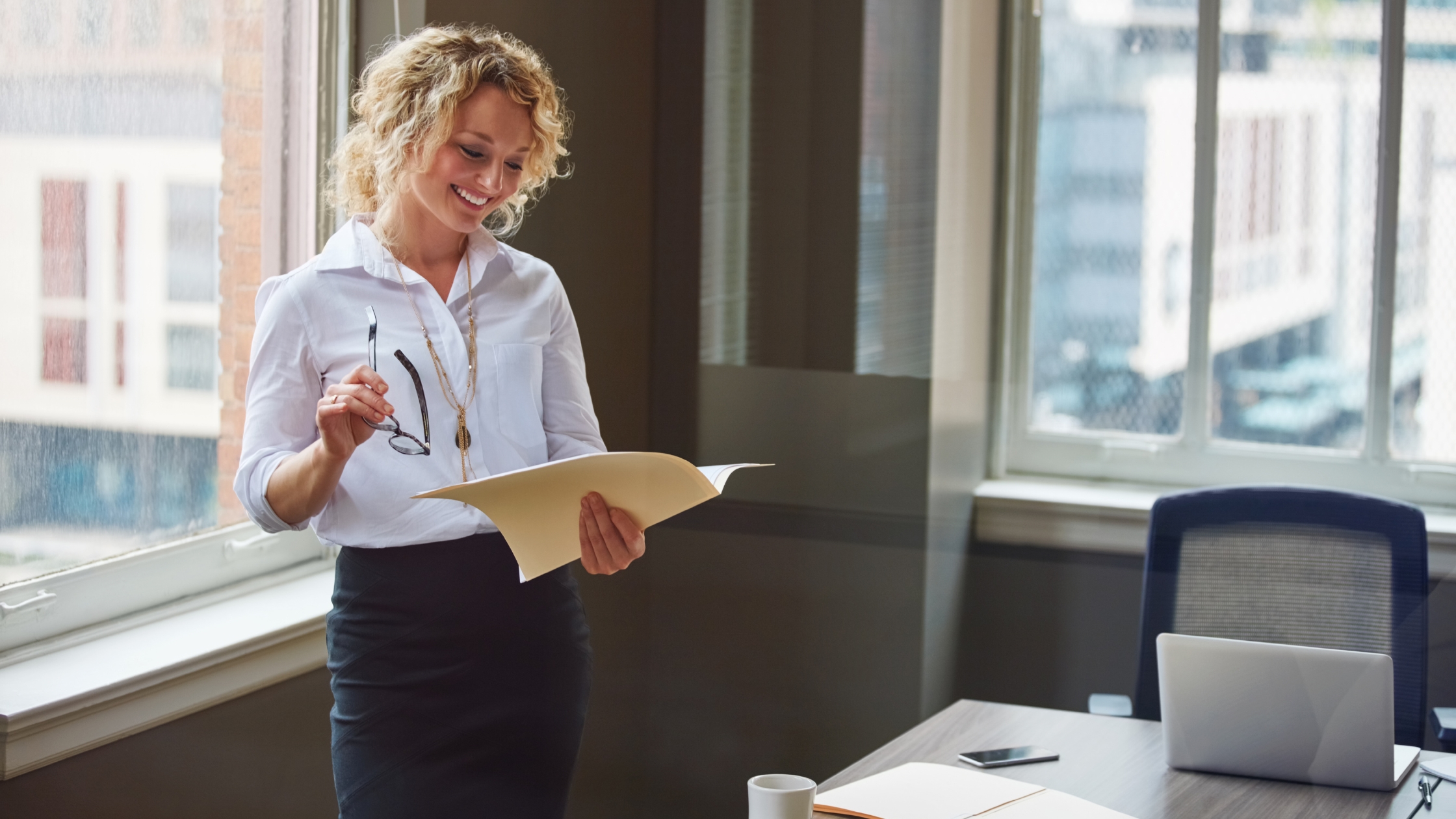 Professional woman smiling while reviewing paperwork in a modern office.